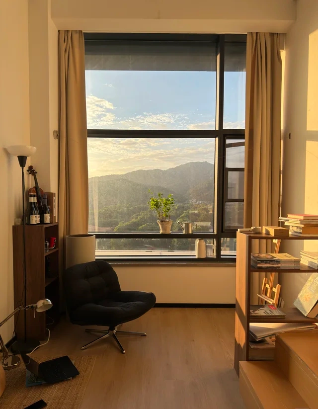 Late afternoon sunlight across a lounge chair, wooden shelves and a mountain-view window